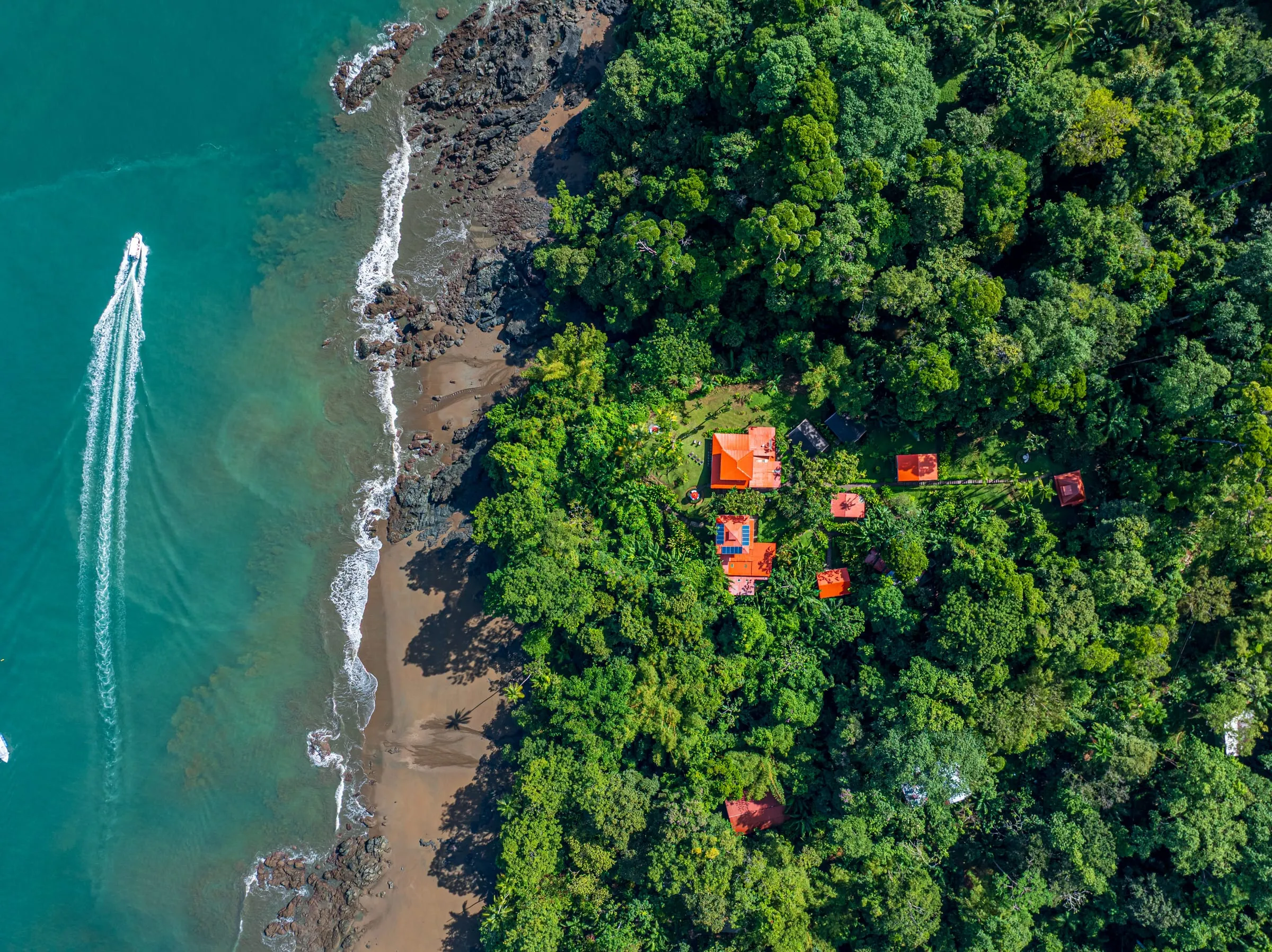 Aerial view of a boat along the coast, with the lodge's red roofs in the forest