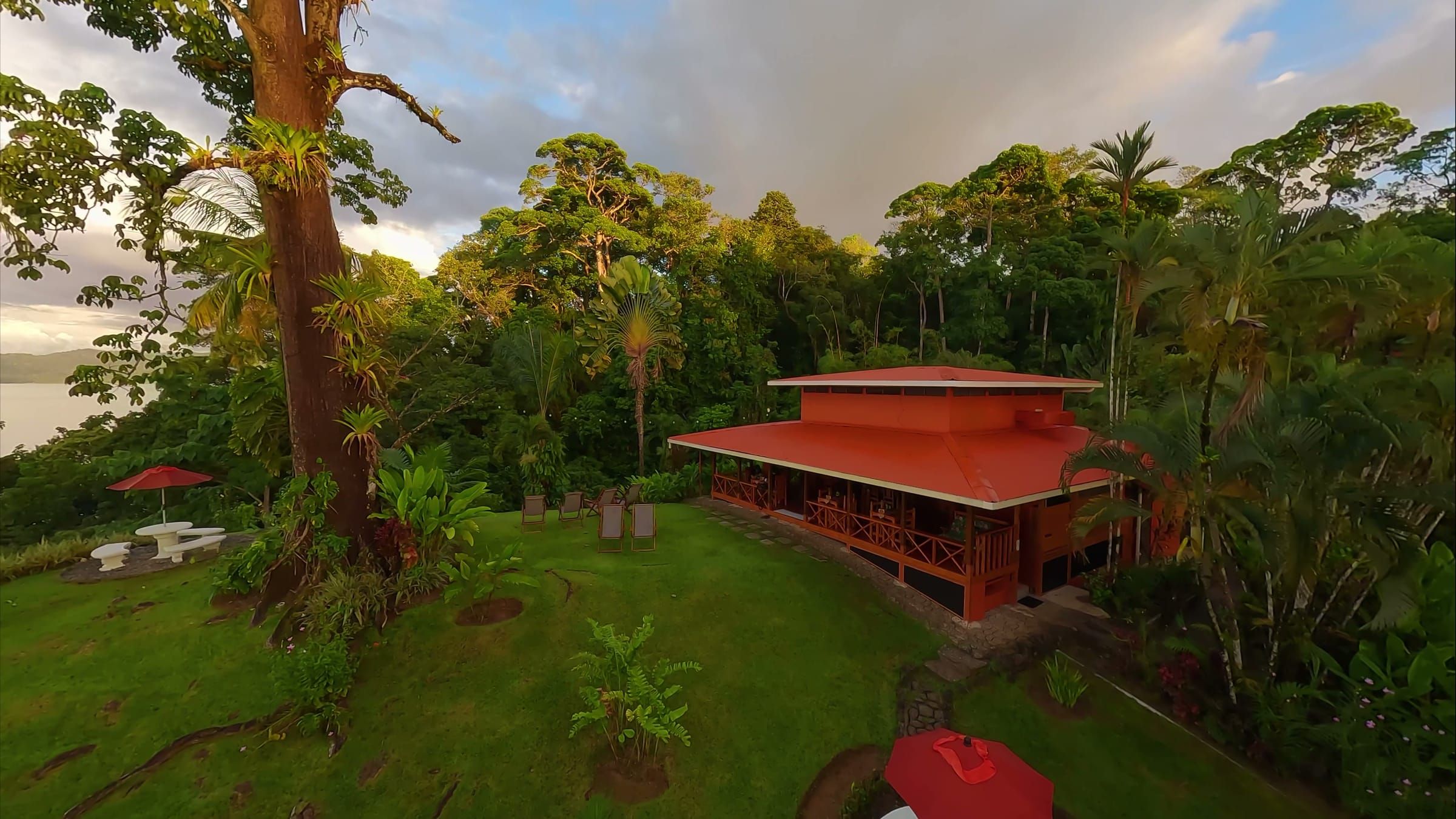 The lodge's red-roofed main house and garden in the rainforest, with the sea beyond
